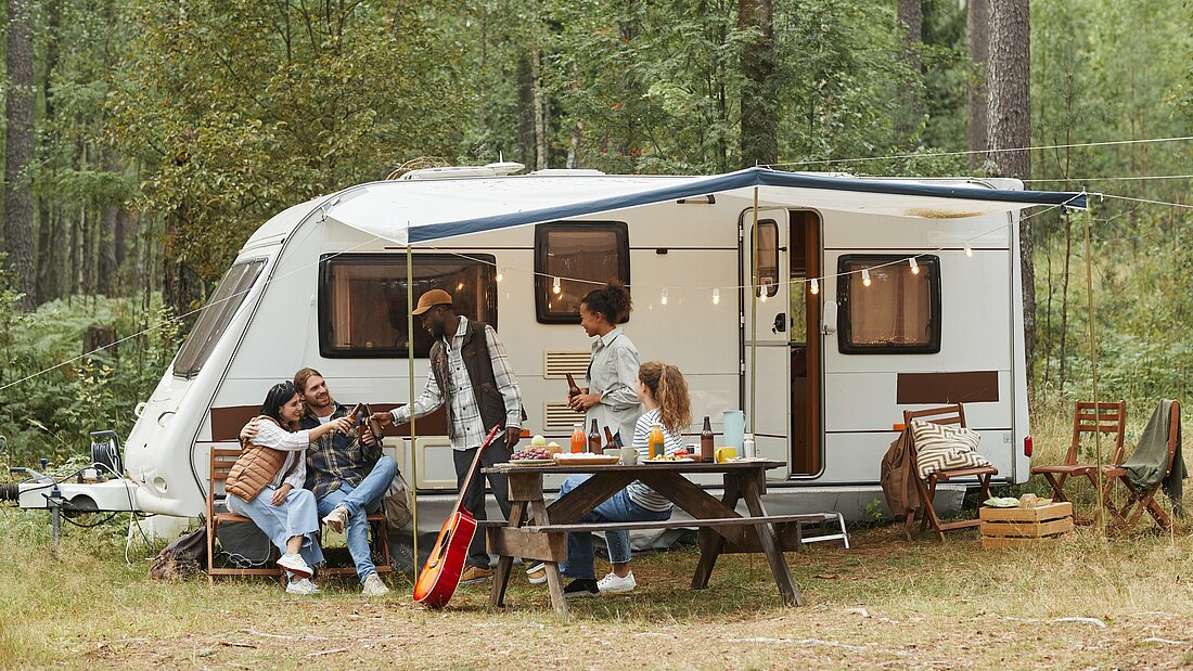 Five young people drinking beer under the canopy of a caravan.