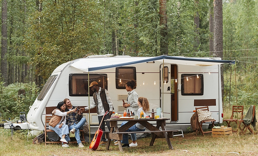 Five young people drinking beer under the canopy of a caravan.