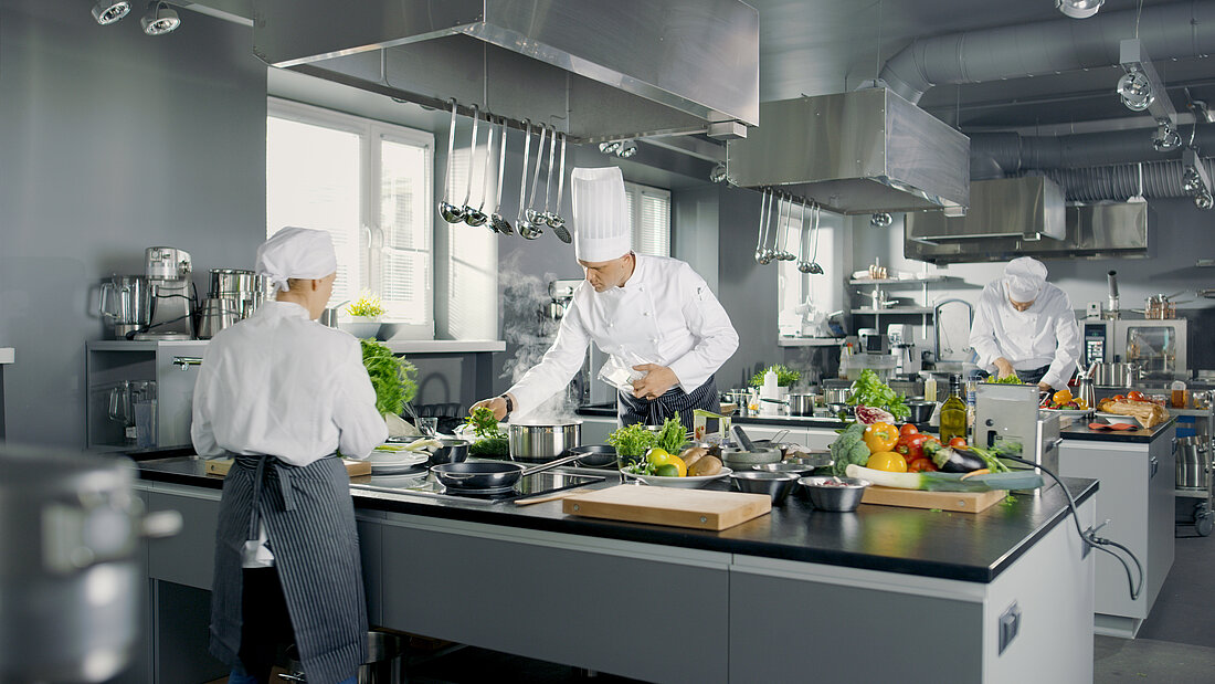 A woman and two men in chef's clothes at work in a commercial kitchen.